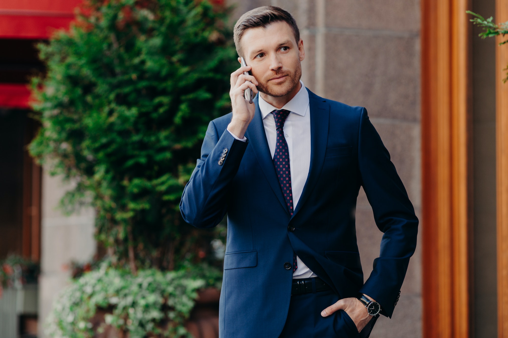 Young male CEO has telephone conversation, looks confidently into distance